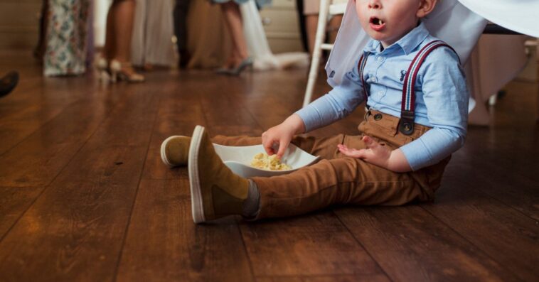 A little boy sits on the floor of a wedding eating food