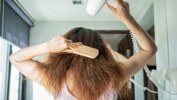 A woman blow dries and combs her long hair