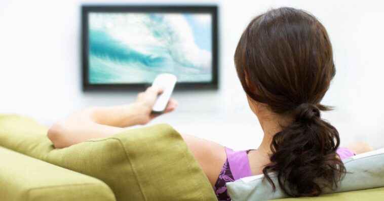 A woman watches TV and uses the remote