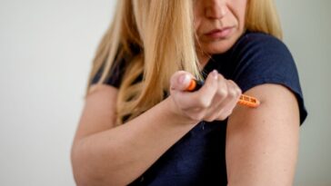A woman stabs herself with an epipen in her arm