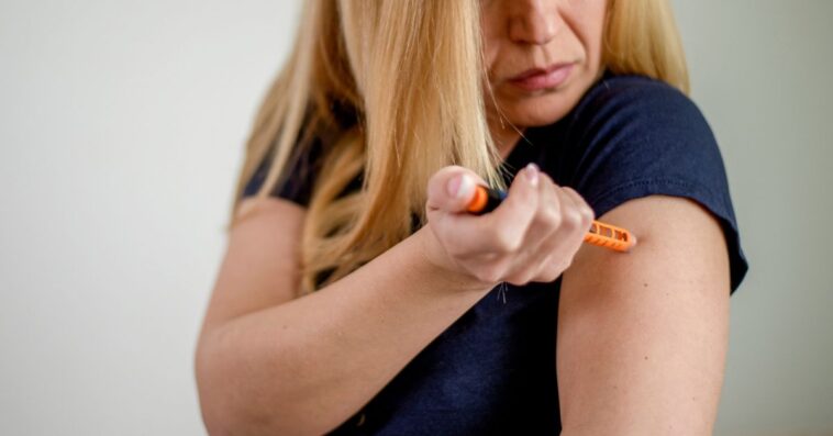 A woman stabs herself with an epipen in her arm