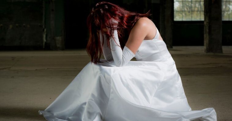 A bride kneels down with her head in her hands