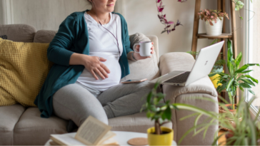 Pregnant woman working from home on a couch with laptop