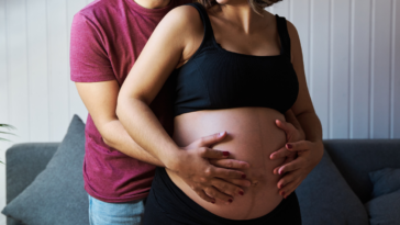 a man standing behind a pregnant woman holding her belly