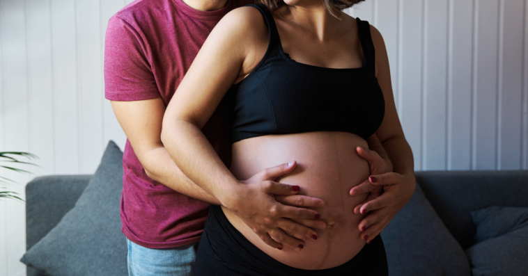 a man standing behind a pregnant woman holding her belly