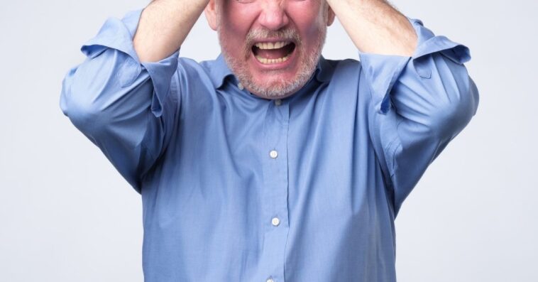 An older, irritated man holds his head in his hands in distress