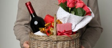 A man presents a basket with wine, roses and candy