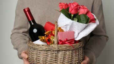A man presents a basket with wine, roses and candy