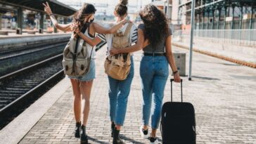 Three women walk arm in arm with luggage