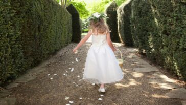 A flower girl runs down a garden path tossing petals