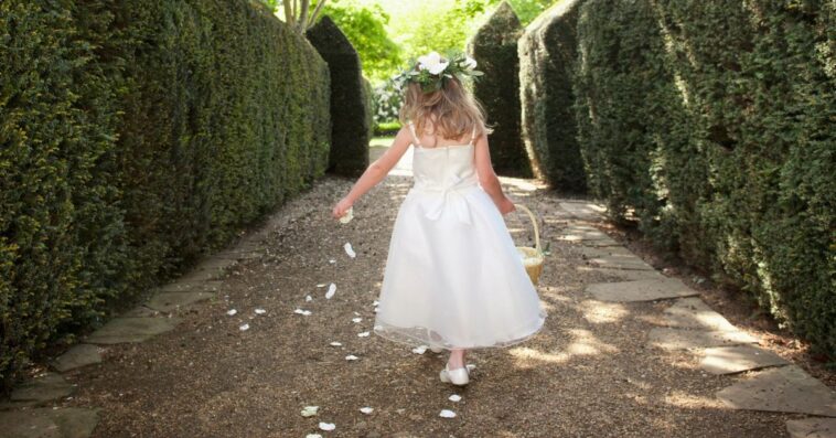 A flower girl runs down a garden path tossing petals