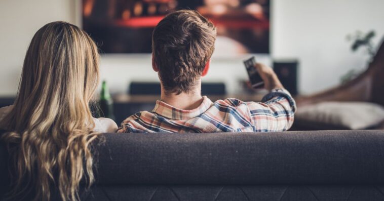 A couple watches a movie, while snuggling on the couch