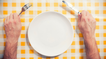 Man holding fork and knife over empty plate