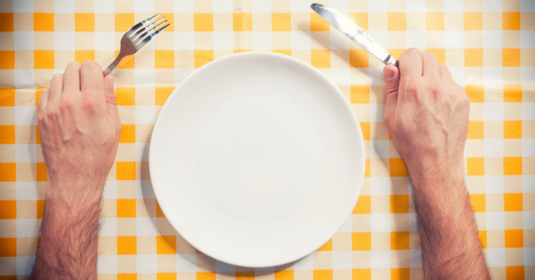 Man holding fork and knife over empty plate