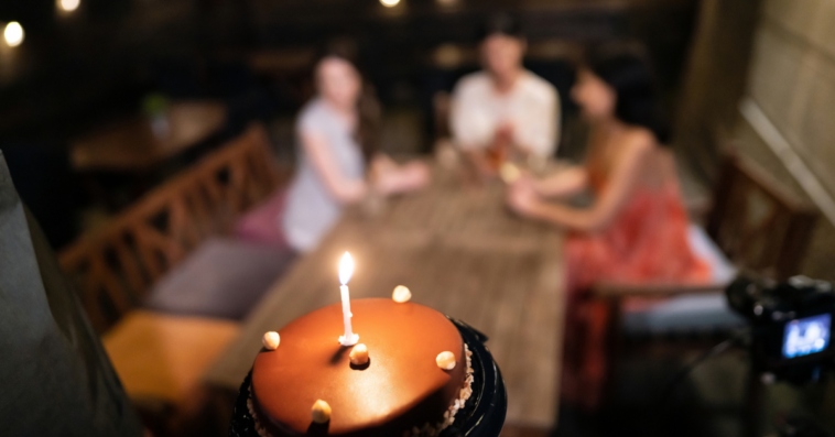 Waiter bringing birthday cake to table of 3 women