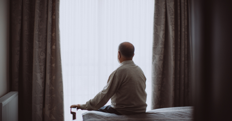 Man sitting on bed looking out window.