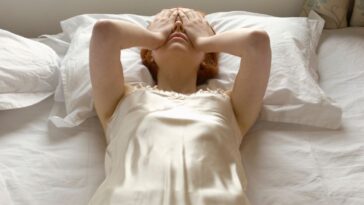 A woman lies back on a bed hands over her eyes