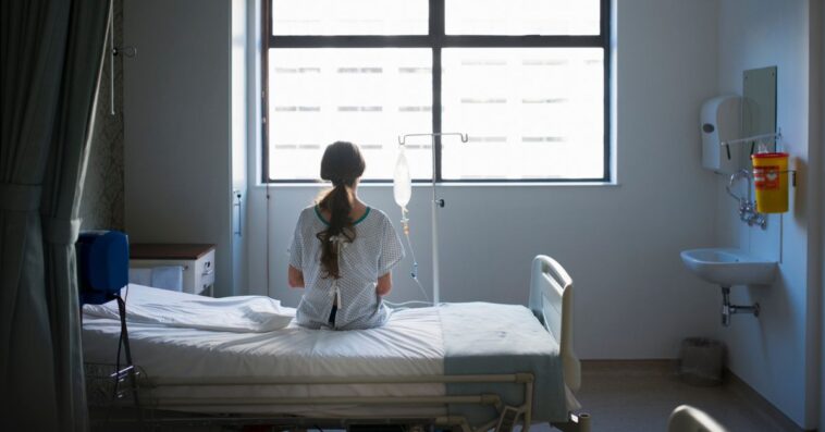 A woman in a hospital bed stares out of the widow