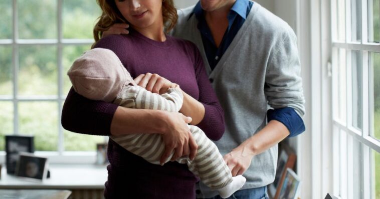 A couple holds their baby and looks on lovingly