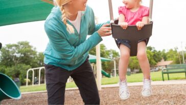 A young woman pushes a little girl in a swing
