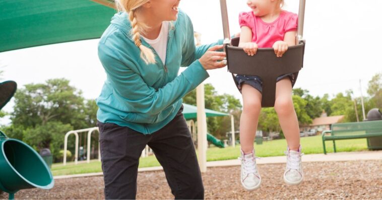 A young woman pushes a little girl in a swing