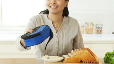 An Indian woman, in a kitchen, offers a lunch bag