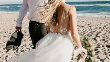 A bride and a groom walk along the beach