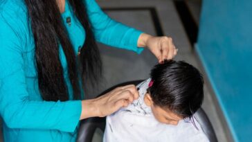 A long haired woman cuts a little boy's hair