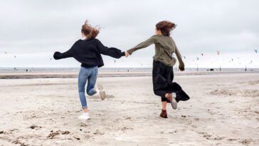 Two young women hold hands and run on the beach