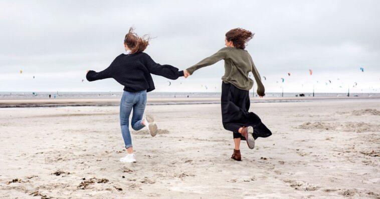 Two young women hold hands and run on the beach