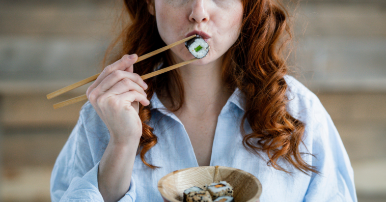 Woman holding a piece of sushi with chopsticks