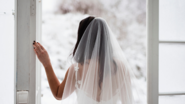 Bride wearing a veil looking out a window.