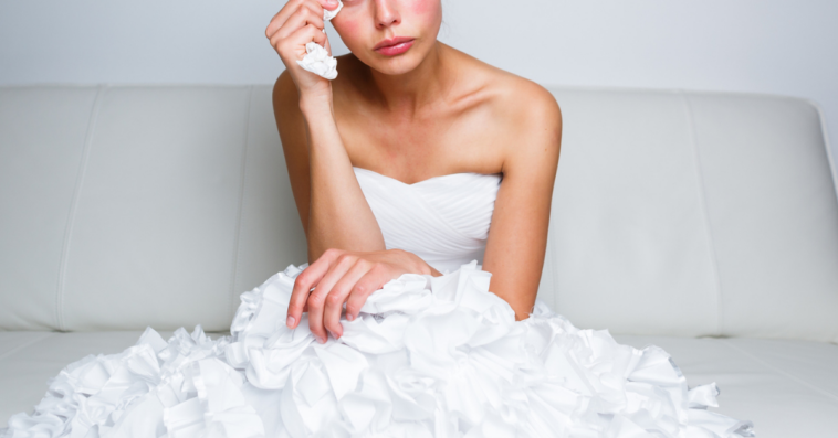 A bride sitting in a white dress wiping away a tear