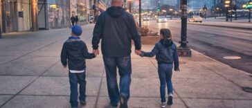 A man walks down the street holding the hands of two children