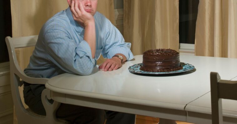 A sad man sits at a table with a chocolate cake