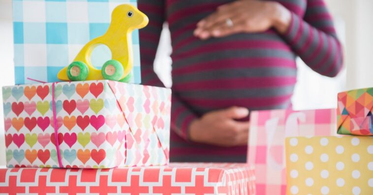 A pregnant woman stands surrounded by gifts at a baby shower