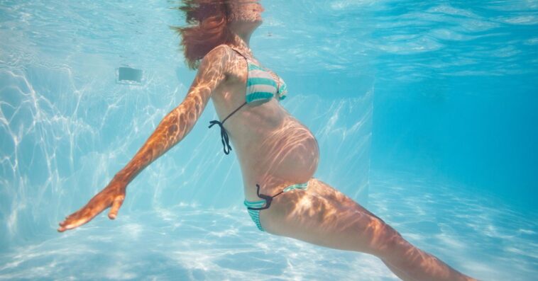 A pregnant woman in a bikini swims underwater