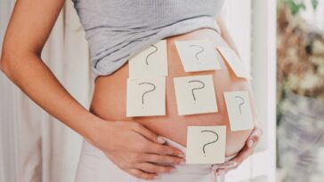 A pregnant woman's belly covered in post-its with question marks