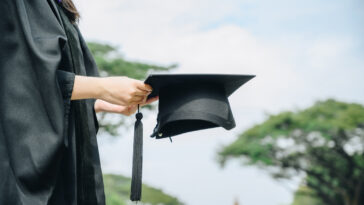 A college graduate holds out their hat
