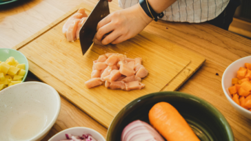 Person cutting chicken on a wooden cutting board