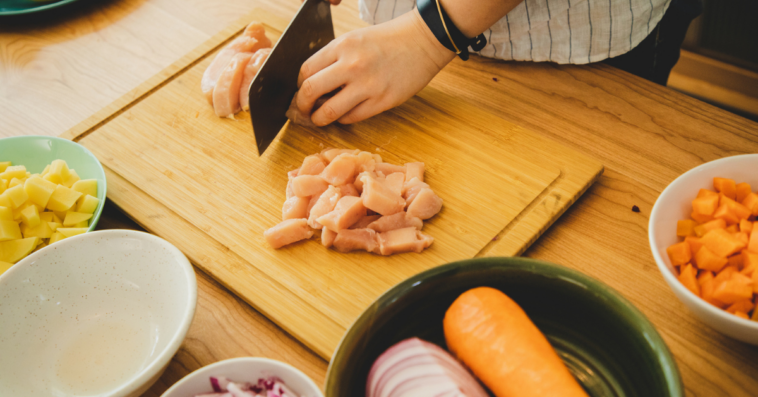 Person cutting chicken on a wooden cutting board