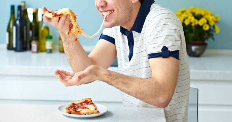 A guy eating a pizza with stringy cheese.