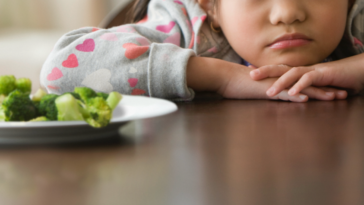 Little girl staring at broccoli.