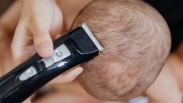 A baby's head is being shaved by electric clippers