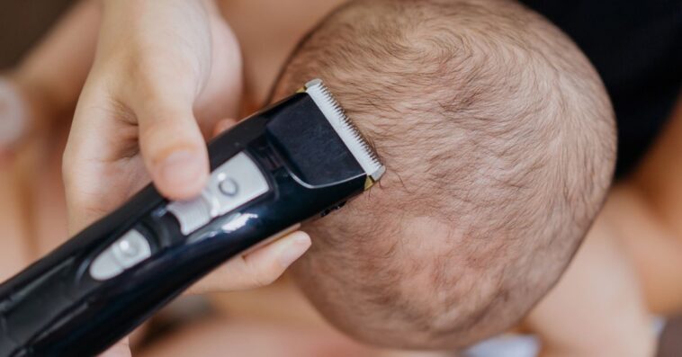 A baby's head is being shaved by electric clippers