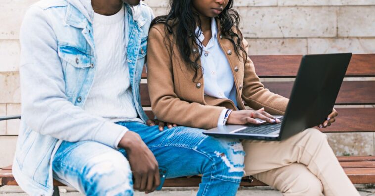 A couple sit on a bench and look at a laptop