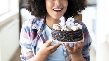 A young girl holds up a chocolate cake with candles saying 16