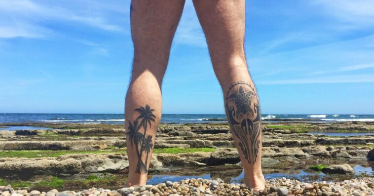 Naked man with tattooed legs looking at the sea on a beach