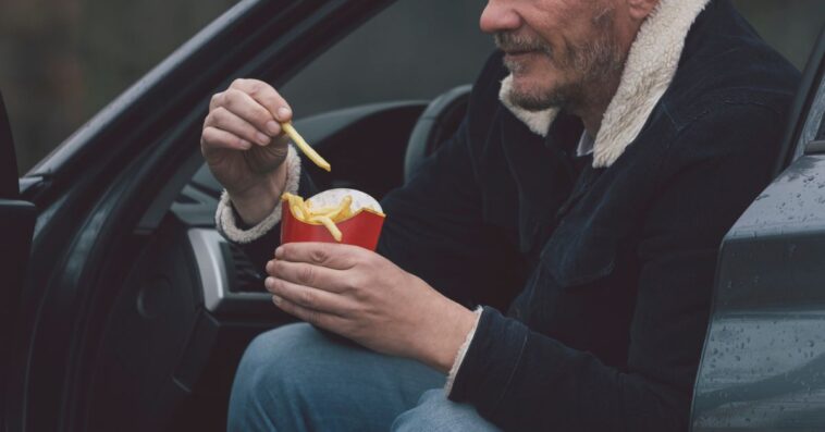 A man eats McDonald's fries in his car