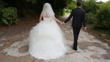A bride and groom walk away from the camera at an outdoor wedding